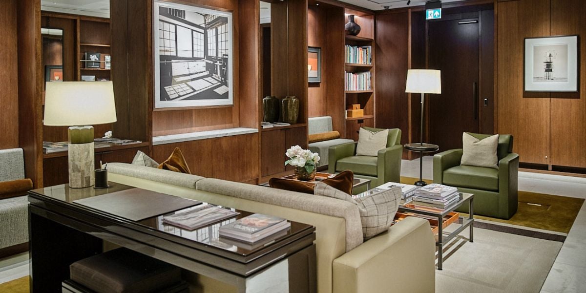 Open plan living room with dark walnut panelling, integrated bookshelves, study desk and lounge seating with green leather armchairs
